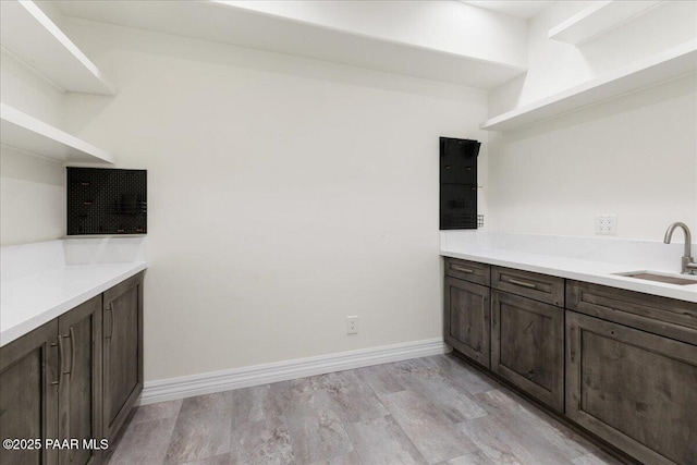 kitchen featuring a sink, baseboards, dark brown cabinets, and light wood-style flooring