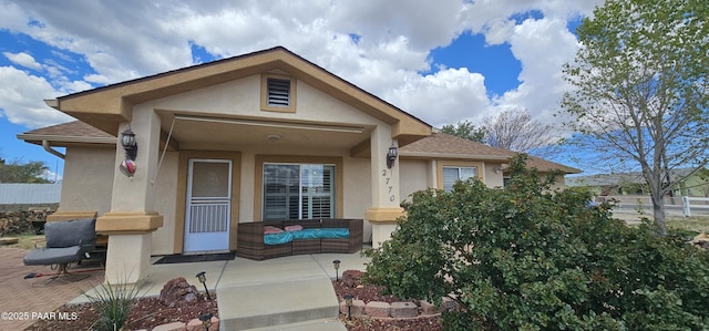 view of front of home with covered porch, fence, a shingled roof, and stucco siding