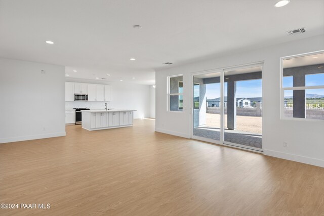 unfurnished living room with plenty of natural light, sink, and light hardwood / wood-style flooring