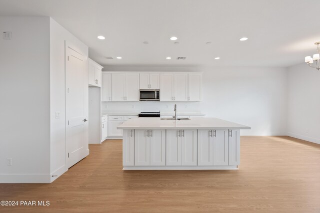 kitchen featuring white cabinets, range, light hardwood / wood-style flooring, and an island with sink