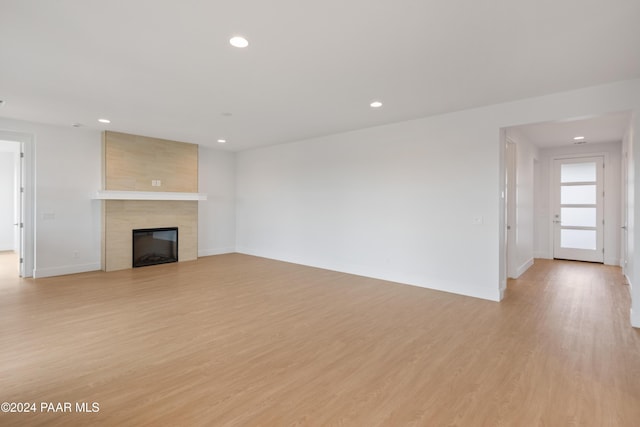 unfurnished living room with a tiled fireplace and light wood-type flooring