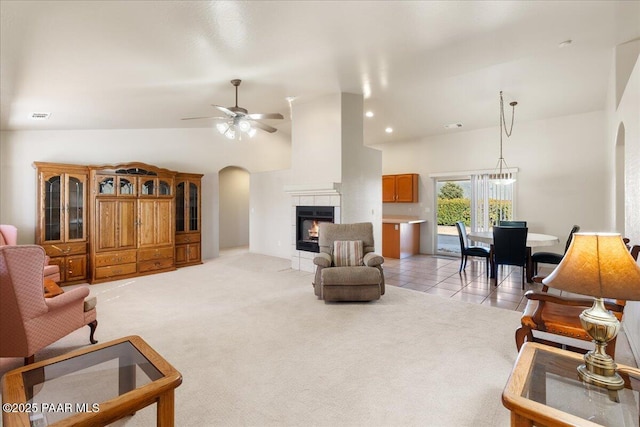 carpeted living room with ceiling fan, high vaulted ceiling, and a tile fireplace