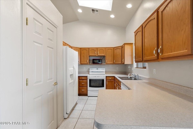 kitchen featuring sink, white appliances, light tile patterned floors, vaulted ceiling with skylight, and kitchen peninsula
