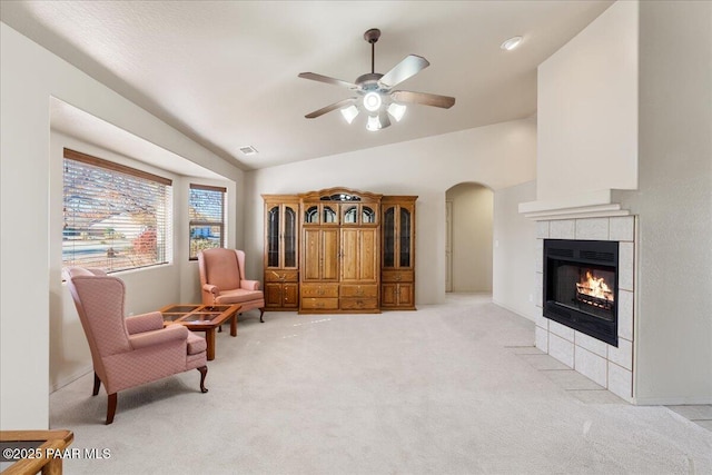 living area featuring a tile fireplace, vaulted ceiling, light colored carpet, and ceiling fan