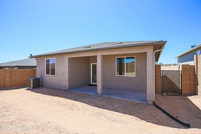 rear view of house with fence, a shingled roof, stucco siding, central AC unit, and a patio area