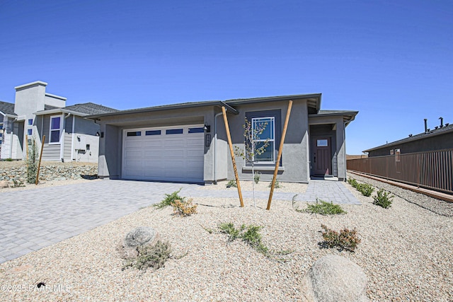 view of front of home featuring a garage, fence, stucco siding, and decorative driveway