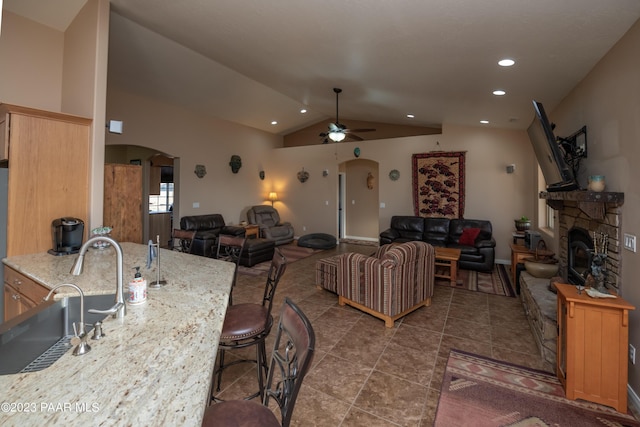 interior space featuring a stone fireplace, ceiling fan, sink, and lofted ceiling