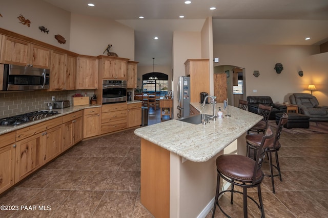 kitchen with light stone countertops, appliances with stainless steel finishes, backsplash, a breakfast bar, and sink