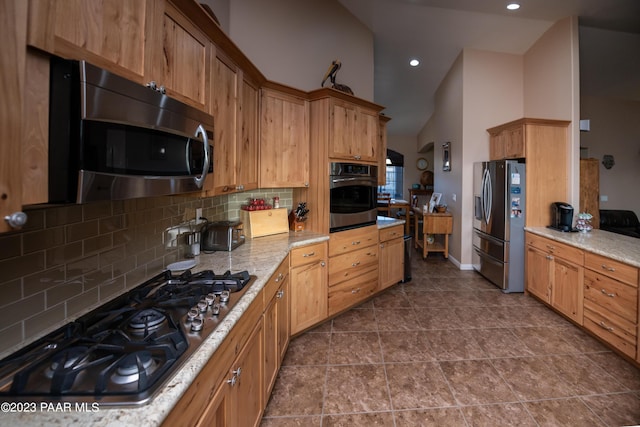 kitchen featuring tasteful backsplash, light stone counters, high vaulted ceiling, dark tile patterned flooring, and appliances with stainless steel finishes