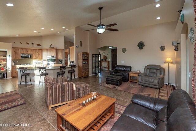 tiled living room with ceiling fan and high vaulted ceiling