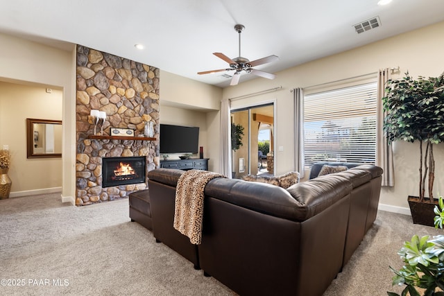 carpeted living room with a stone fireplace and ceiling fan