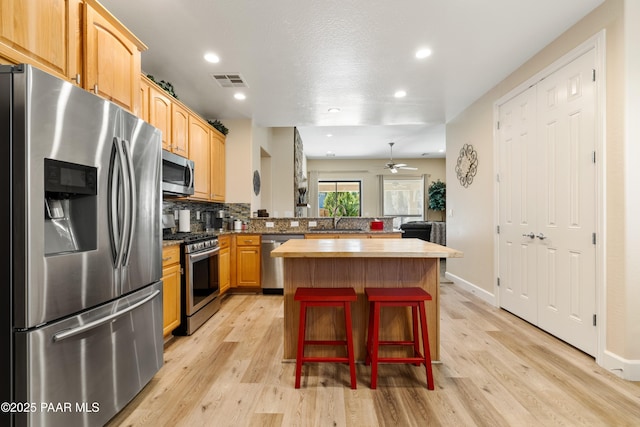 kitchen featuring a kitchen island, appliances with stainless steel finishes, butcher block countertops, a kitchen breakfast bar, and light wood-type flooring