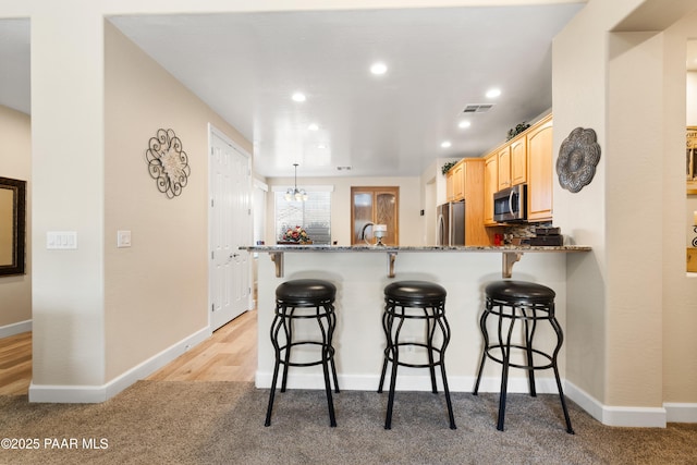 kitchen featuring stainless steel appliances, light carpet, a kitchen breakfast bar, and kitchen peninsula