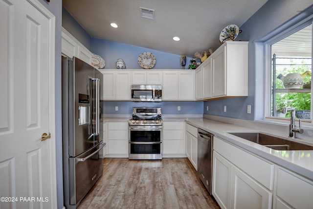 kitchen with sink, light hardwood / wood-style floors, vaulted ceiling, white cabinets, and appliances with stainless steel finishes