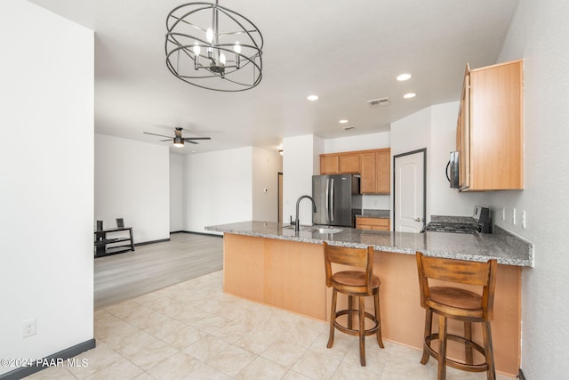 kitchen with stone counters, kitchen peninsula, appliances with stainless steel finishes, ceiling fan with notable chandelier, and light wood-type flooring