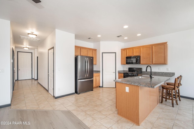 kitchen with black appliances, sink, dark stone countertops, kitchen peninsula, and a breakfast bar area