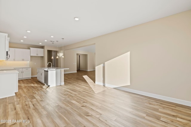 kitchen with white cabinetry, sink, hanging light fixtures, a center island with sink, and light wood-type flooring