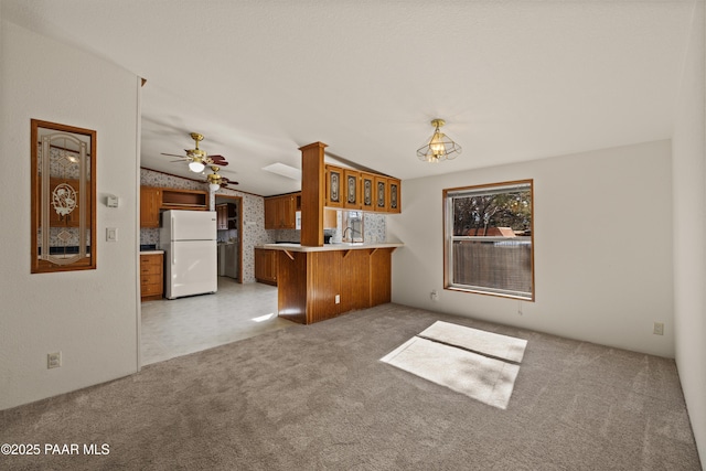 kitchen with lofted ceiling, a breakfast bar area, white refrigerator, light colored carpet, and kitchen peninsula