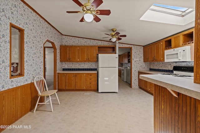 kitchen featuring ceiling fan, white appliances, ornamental molding, and vaulted ceiling with skylight