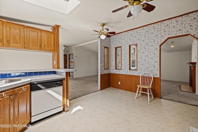 kitchen featuring a skylight, ornamental molding, wooden walls, white dishwasher, and ceiling fan