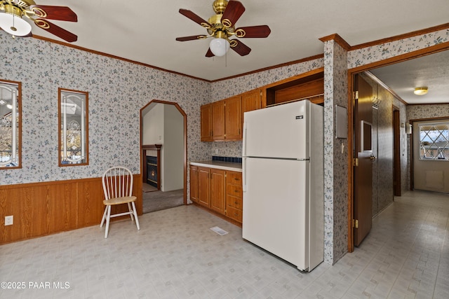 kitchen featuring wooden walls, ornamental molding, ceiling fan, and white fridge