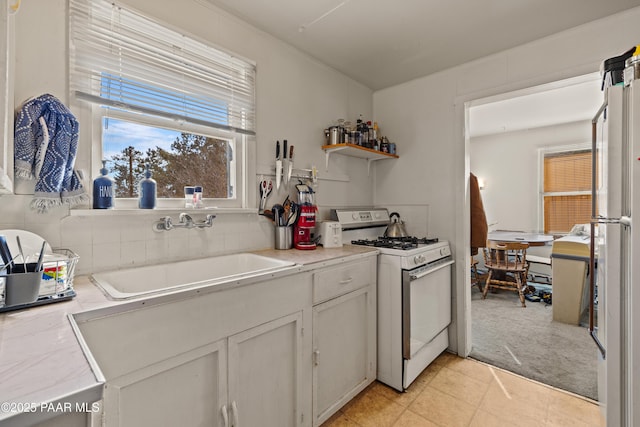 kitchen with light colored carpet, white gas range, sink, and white cabinets