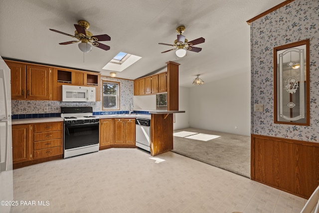 kitchen featuring sink, white appliances, ceiling fan, lofted ceiling with skylight, and kitchen peninsula