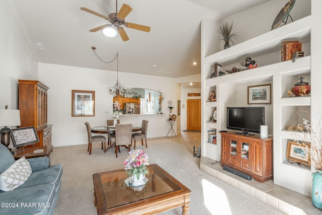 carpeted living room featuring vaulted ceiling, built in shelves, and ceiling fan with notable chandelier