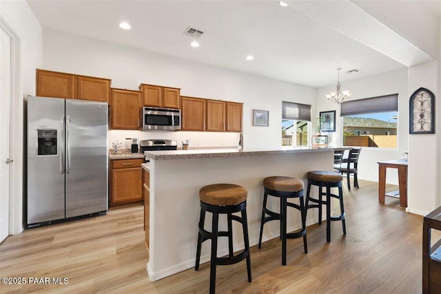 kitchen with hanging light fixtures, a kitchen bar, a kitchen island with sink, and appliances with stainless steel finishes