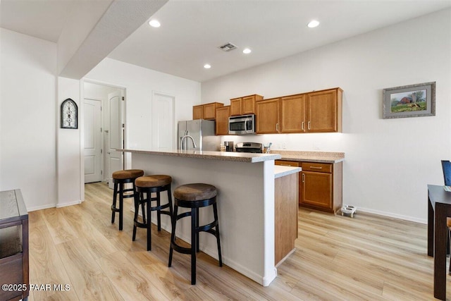 kitchen featuring a center island with sink, a breakfast bar, light hardwood / wood-style floors, and stainless steel appliances