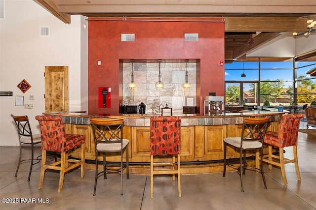 bar with backsplash, beamed ceiling, concrete floors, and decorative light fixtures