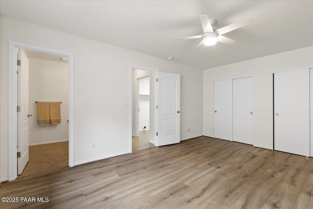 unfurnished bedroom with two closets, baseboards, and wood finished floors