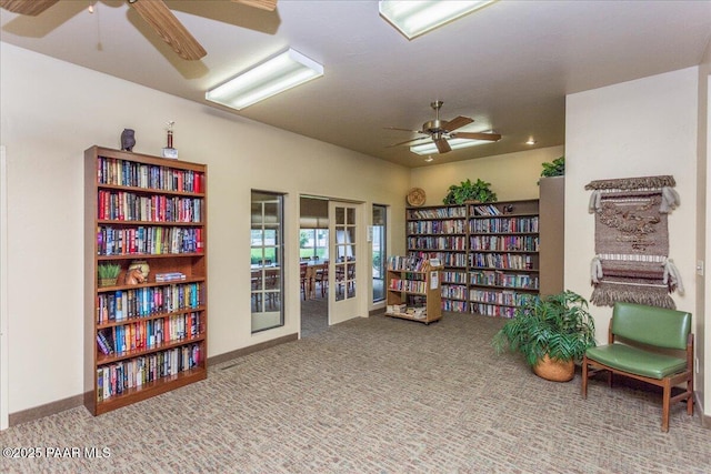 living area featuring baseboards, carpet, bookshelves, french doors, and a ceiling fan