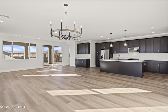 kitchen featuring a center island with sink, hanging light fixtures, light wood-type flooring, appliances with stainless steel finishes, and a notable chandelier