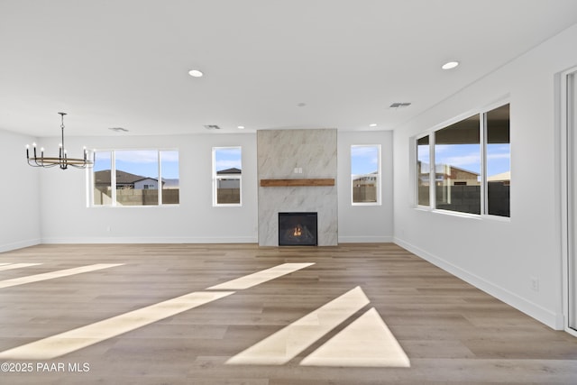 unfurnished living room with a notable chandelier, plenty of natural light, a fireplace, and light hardwood / wood-style flooring