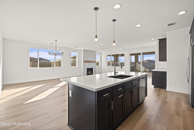 kitchen with decorative light fixtures, a kitchen island with sink, light hardwood / wood-style floors, and sink