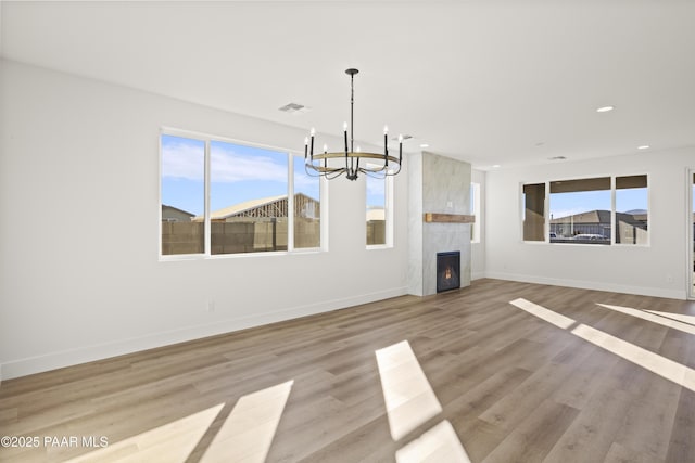 unfurnished living room with light hardwood / wood-style flooring, a fireplace, a wealth of natural light, and a chandelier