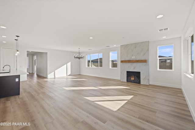 unfurnished living room featuring a chandelier, a large fireplace, light hardwood / wood-style flooring, and sink