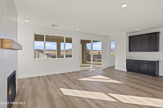 unfurnished living room with a tile fireplace, a wealth of natural light, and light hardwood / wood-style floors