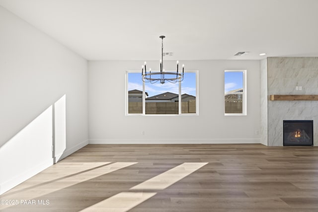 unfurnished dining area with a premium fireplace, wood-type flooring, and a notable chandelier