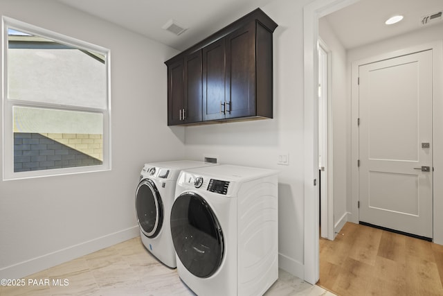 clothes washing area featuring separate washer and dryer, light hardwood / wood-style flooring, and cabinets