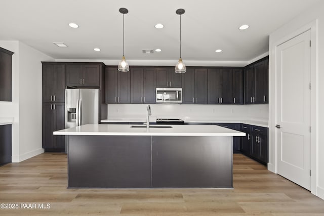 kitchen featuring a center island with sink, hanging light fixtures, sink, and appliances with stainless steel finishes