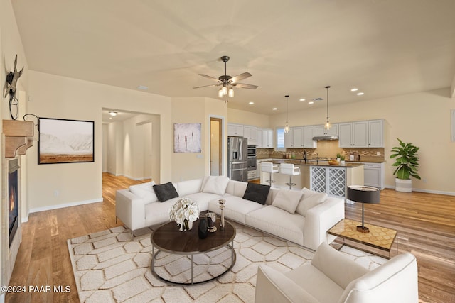 unfurnished living room featuring ceiling fan, sink, and light wood-type flooring