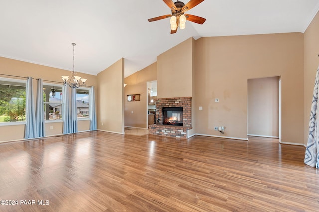 unfurnished living room with wood finished floors, baseboards, high vaulted ceiling, a brick fireplace, and ceiling fan with notable chandelier