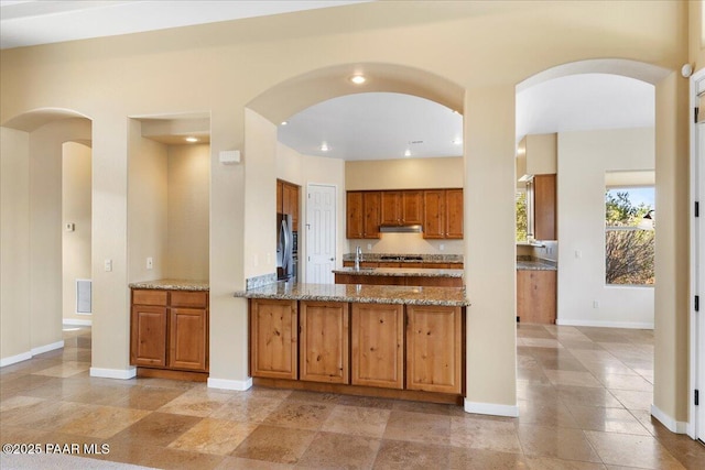 5560 W Halcyone Cir, Prescott, AZ 86305 - kitchen featuring light stone counters, a peninsula, baseboards, freestanding refrigerator, and brown cabinetry