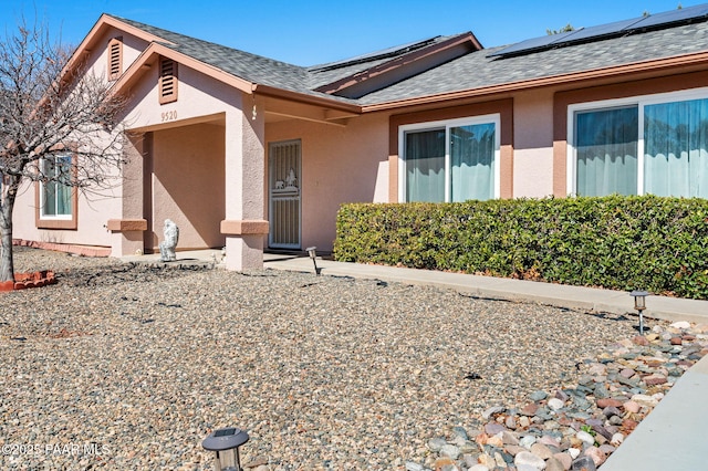 exterior space featuring a shingled roof, roof mounted solar panels, and stucco siding