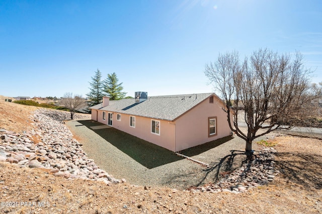 view of side of property with central AC unit, roof with shingles, a chimney, and stucco siding