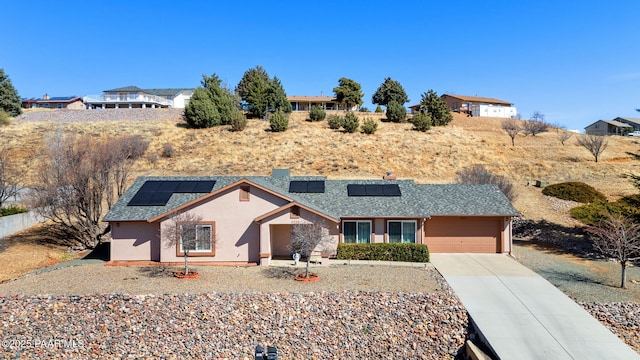 view of front of property with a garage, a shingled roof, concrete driveway, roof mounted solar panels, and stucco siding