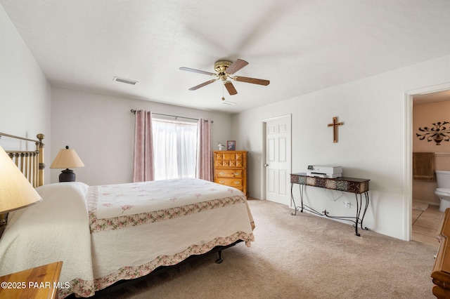 carpeted bedroom with ensuite bathroom, visible vents, and a ceiling fan