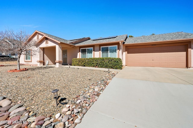 ranch-style home with stucco siding, a shingled roof, roof mounted solar panels, a garage, and driveway